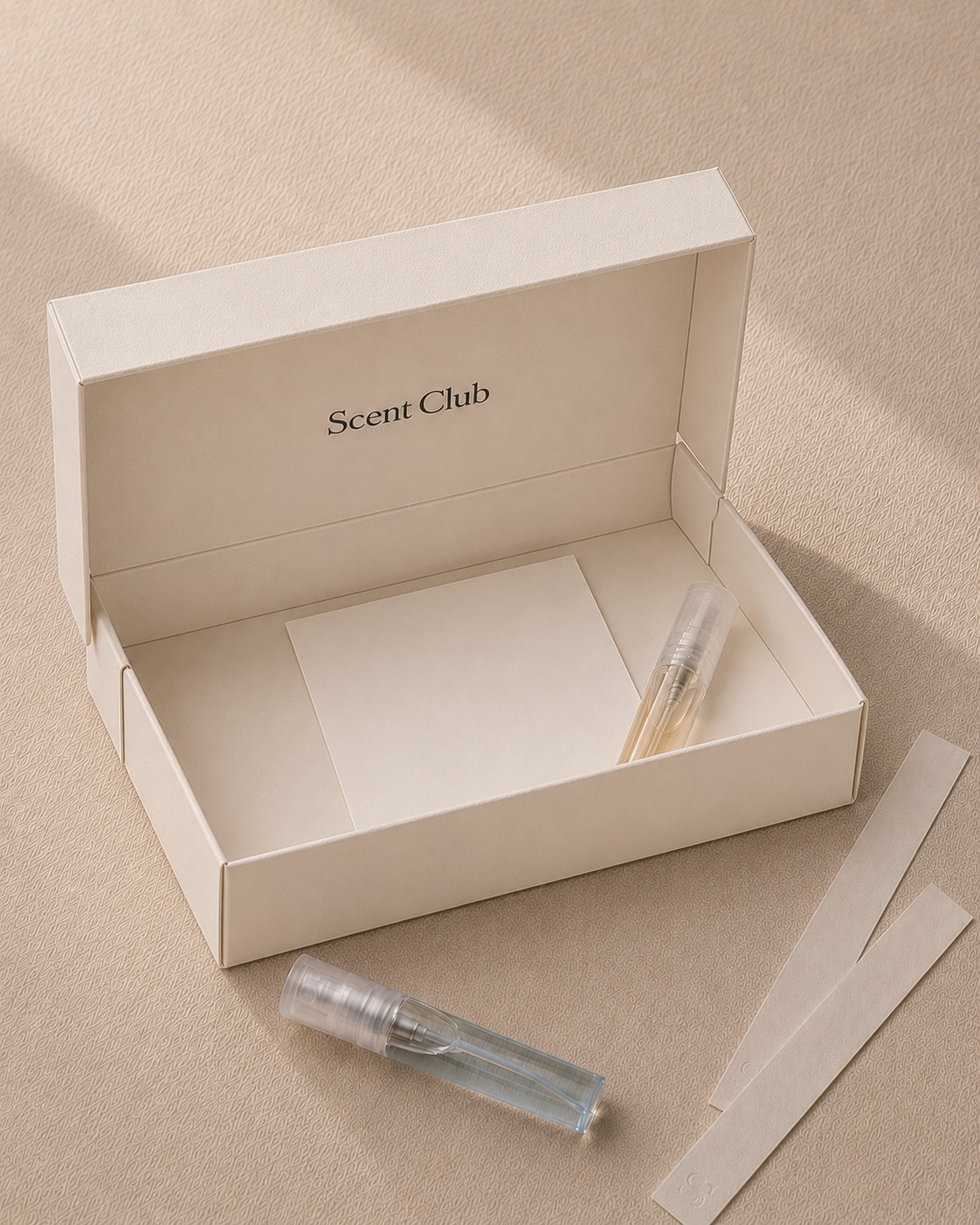 Caja ScentClub abierta con dos decants Scent2Go de 5ml, una tarjeta de selección y blotters sobre papel crema; comunica entrada simple al club.